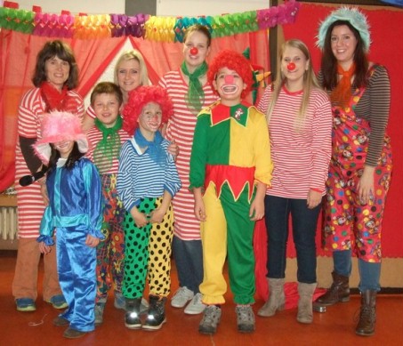 Das Bild zeigt Studierende und Schülerinnen als Clowns verkleidet vor der Zirkuskulisse