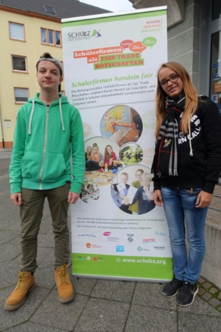 Auf diesem Foto sieht man zwei Schüler der LVR-Schule vor dem Plakat „Schülerfirmen als Fairtrade-Botschafter“