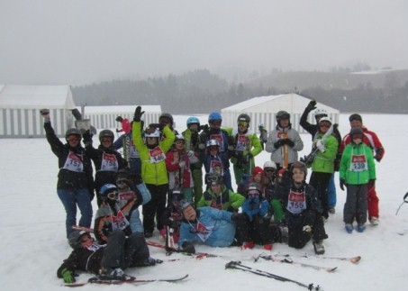 Abgebildet ist ein Gruppenfoto nach dem Skirennen im Schnee auf der Piste.