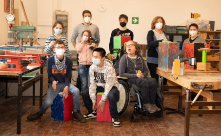 Foto: Schulleitung, Lehrkraft und 6 Schüler*innen, zum Teil im Rollstuhl sitzend im Werkraum mit selbst gebauten Cajons